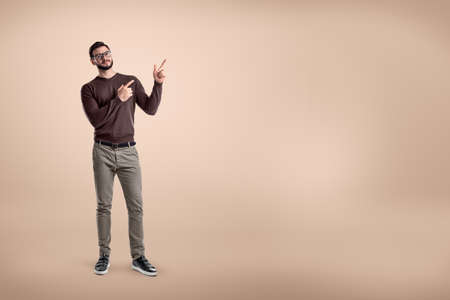 Young smiling man wearing casual clothes and pointing up on beige backgroundの写真素材