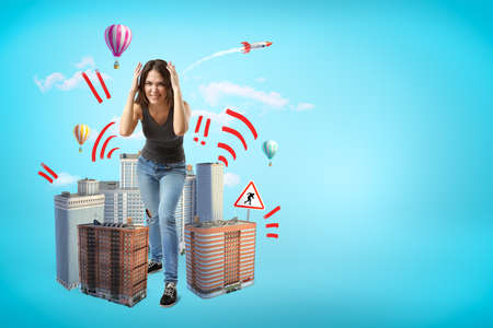 Young girl in casual clothes making brain explosion gesture with city skyscrapers and hot air balloons on blue backgroundの写真素材