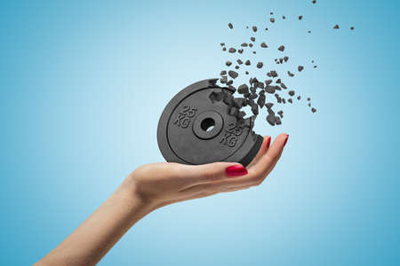Side closeup of womans hand facing up and holding black 25kg weight plate that is dissolving in...