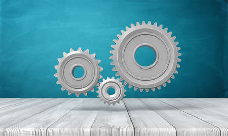 3d rendering of light-grey metal gearwheels on wooden surface on blue wall background.の写真素材