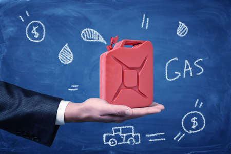 Male hand holding red gasoline can with cartoon drawings on blue backgroundの写真素材