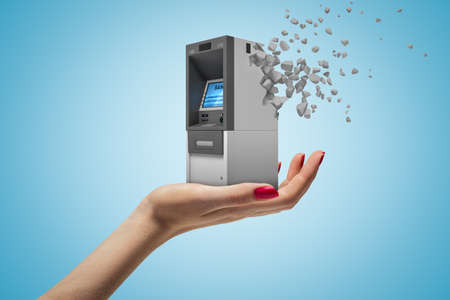 Side closeup of womans hand facing up and holding small ATM which has started to dissolve into pieces on light-blue background.の写真素材