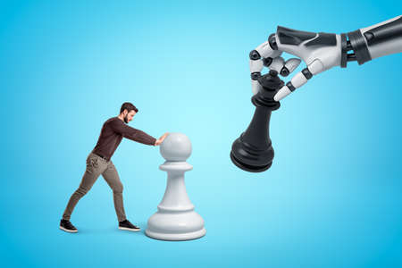 Young man in casual clothes playing chess with big robotic hand on blue backgroundの写真素材
