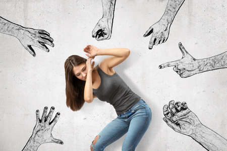Young girl bending down covering her face with her hands trying to protect herself from mens fists, finger guns and hands pointing at her.の写真素材