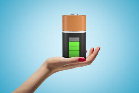 Female hand holding fully charged battery on blue backgroundの写真素材