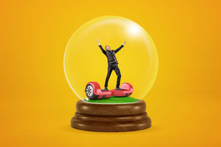 Happy businessman raising arms on red hoverboard in a snow globe on yellow backgroundの写真素材