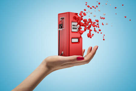 Female hand holding red filling station shattering into pieces on blue backgroundの写真素材