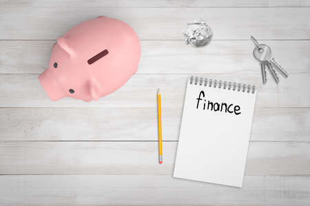 3d rendering of notepad with word Finance written in it, pencil, piggy bank, crumpled piece of paper, and keys on wooden desk, viewed from above.の写真素材
