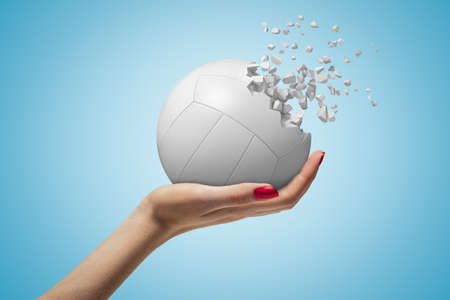 Female hand holding white volleyball ball shattering into pieces on blue backgroundの写真素材