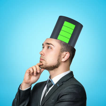 Crop image of businessman in half-turn thinking with hand at chin and fully charged battery emerging from top of his head.の写真素材