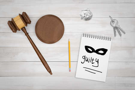 3d rendering of round wooden block, brown wooden gavel, keys and pencil with Guilty sign and mask drawn in a notebook on white wooden background.の写真素材