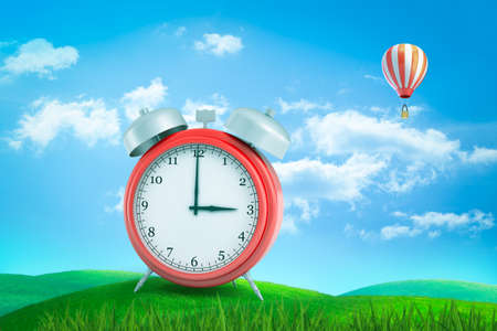 3d rendering of red retro alarm clock showing 3 oclock standing on green grass under blue sky with hot air balloon in distance.の写真素材