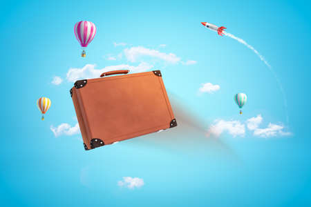 3d rendering of brown travel case in blue sky with hot air balloons and space rocket in distance.の写真素材