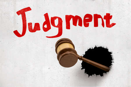 3d rendering of brown wooden gavel breaking white wall with red 'Judgement' sign on white background. Digital art. Objects and materials. Judgement and punishment.の写真素材