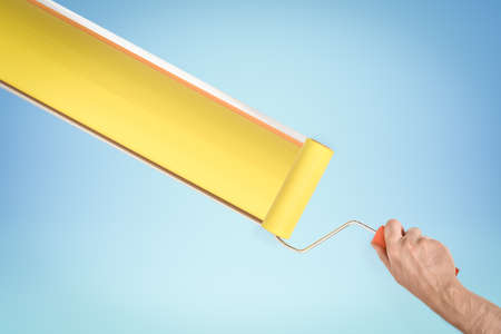 Hand painting yellow stripe with paint roller on blue backgroundの写真素材