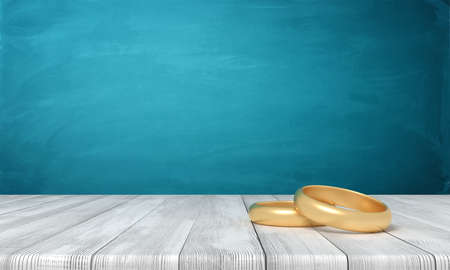 3d rendering of two gold rings lying on wooden table near blue wall with a lot of copy space.の写真素材
