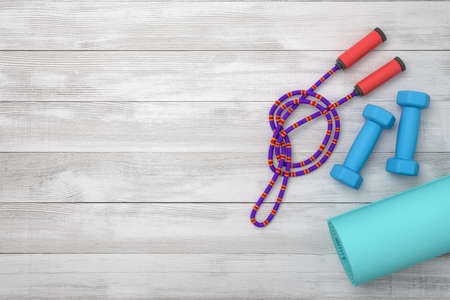 3d rendering of violet jumping rope, blue dumbbells and fitness mat on wooden backgroundの写真素材