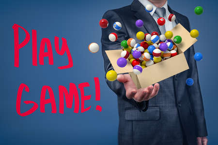 Businessman holding cardboard box filled with colorful pool and billiard balls and Play game sign on blue backgroundの写真素材