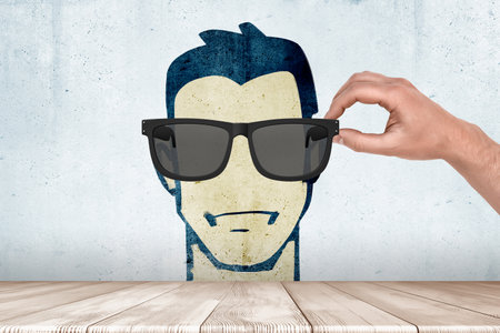 Hand putting sunglasses on wall drawing faceの写真素材