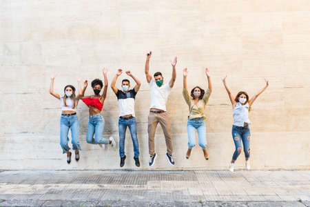 Young friends jumping together while wearing face mask outdoor - Happy people having fun in city...