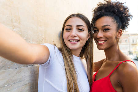 two interracial women taking selfies in street. multiracial girls have fun. Two girls hugging and...