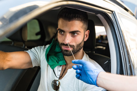 taking a nasal swab from a man in car to test for coronavirus infection - A healthcare worker operates a check swab for Covid-19 to a man sitting inside his carの写真素材