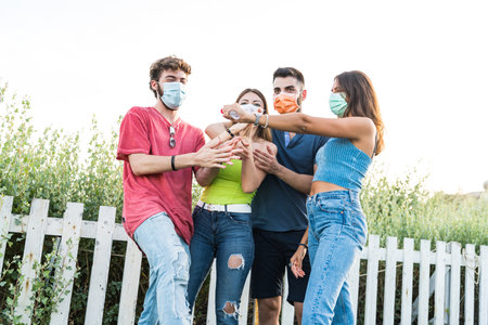 Group of young people wearing protective mask using sanitizing gel together against the coronavirus (covid-19) pandemic - Happy friendship and new normal concept with young people having fun togetherの写真素材