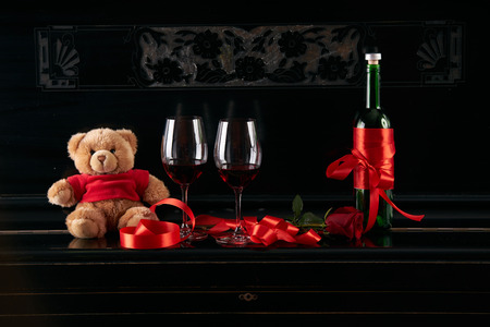 Wine bottle and two wineglasses decorated with red rose, teddy bear toy and  ribbon on a dark background. Valentine's day theme conceptの写真素材