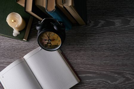 Top view af blank notebook, books, alarm clock and candle on wooden table. Education, knowledge concept with copy spaceの写真素材