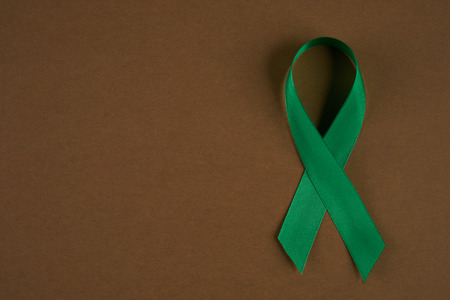 Green awareness ribbon on brown background. Symbol of Mental Health. Top vew with copy spaceの写真素材
