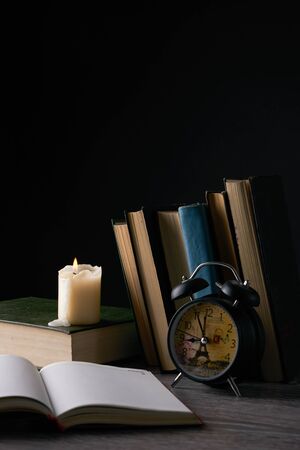 Blank notebook, books, alarm clock and candle on wooden table against black . Education, knowledge conceptの写真素材