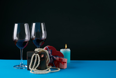 Two wine glasses with gift boxes, candle and pearl necklace on dark background. Love present card concept with copy space. Valentine's day themeの写真素材