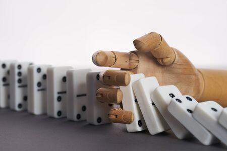 Wooden hand trying to stop toppling dominoes on table. Chain Reactionの写真素材