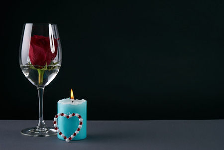 Wineglass with rosebud inside, candle and heart on dark background. Love card concept with copy space. Valentine's day themeの写真素材