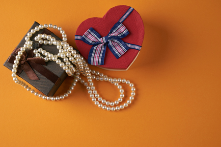 Pearl necklace with heart shaped gift box on a orange background, Love present card concept. Valentine's day themeの写真素材