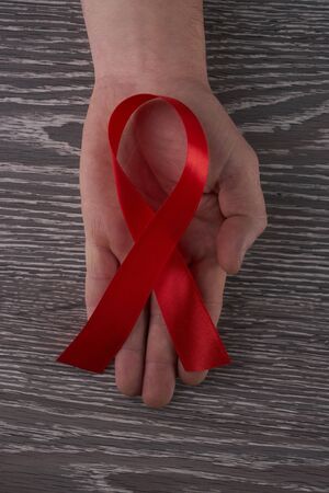 Healthcare and medicine concept -  hand holding red AIDS HIV awareness ribbon against gray wooden backgroundの写真素材