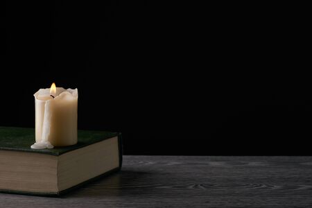 Book and candle on wooden table against dark background. Education, knowledge concept with copy spaceの写真素材
