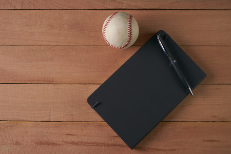 Notebook with pen and baseball ball on an wood table, top viewの写真素材