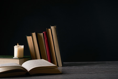 Books and candle on wooden table against dark background. Education, knowledge concept with copy spaceの写真素材