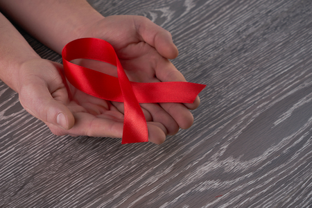 Healthcare and medicine concept -  hands holding red AIDS HIV awareness ribbon against gray wooden...