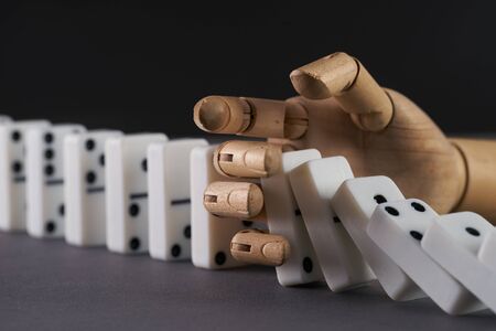 Wooden hand trying to stop toppling dominoes on table. Chain Reactionの写真素材