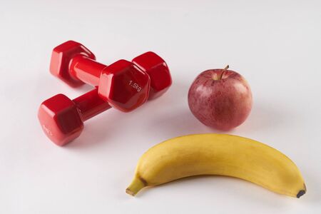 Plastic coated dumbells and fresh fruits: banana, apple on white backgroundの写真素材