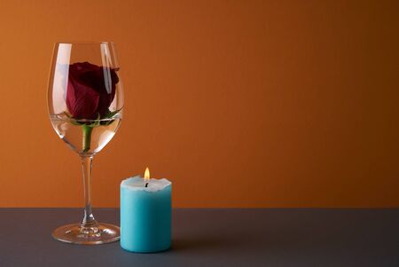 Wineglass with rosebud inside, candle and heart on orange background. Love card concept with copy space. Valentine's day themeの写真素材