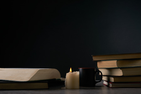 Books and candle on wooden table against dark background. Education, knowledge concept with copy spaceの写真素材