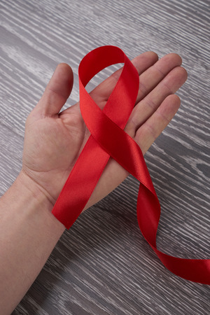 Healthcare and medicine concept -  hand holding red AIDS HIV awareness ribbon against gray wooden backgroundの写真素材