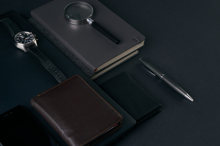 Close up of gentleman set. Magnifying glass, mobile phone, notebook, pen, watch, purse on dark background. Copy spaceの写真素材