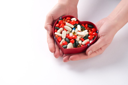 Hands holding different colored medicine and types of pills in heart shaped box on white background. Copy spaceの写真素材