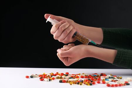 female hands with medical syringe with drug and different colored medicine and types of pills . Doing inject in vein. On dark background.の写真素材