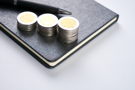 Business concept. Closeup stack of coins, pen and notepad on white background.の写真素材