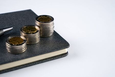 Business concept. Closeup stack of coins, pen and notepad on white background.の写真素材